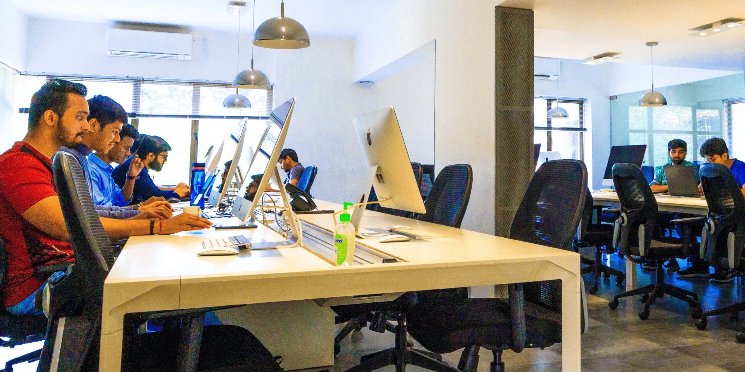 Modern and spacious office environment showcasing team members deeply engaged in their work, with some intensely focused on their computer screens and others in active discussion, exemplifying Samespace's vibrant and dedicated work culture.